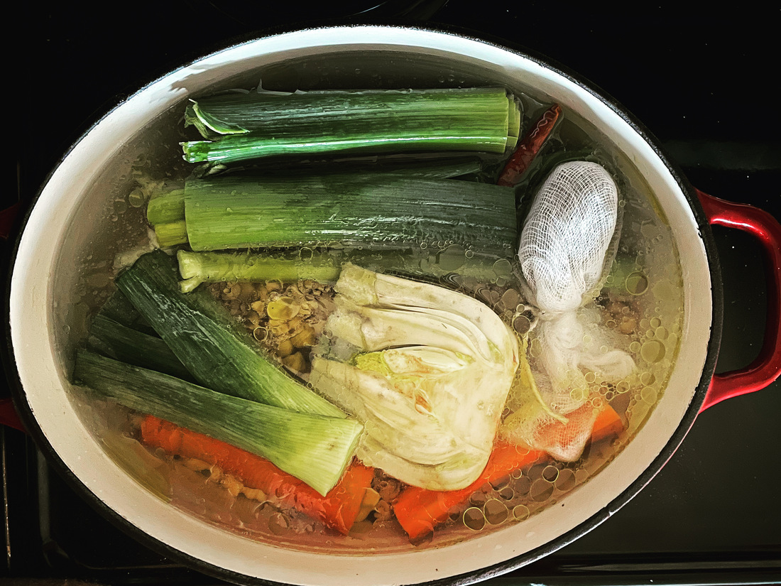 An overhead picture of a cast iron pot filled with liquid, various vegetables, and chickpeas for braising